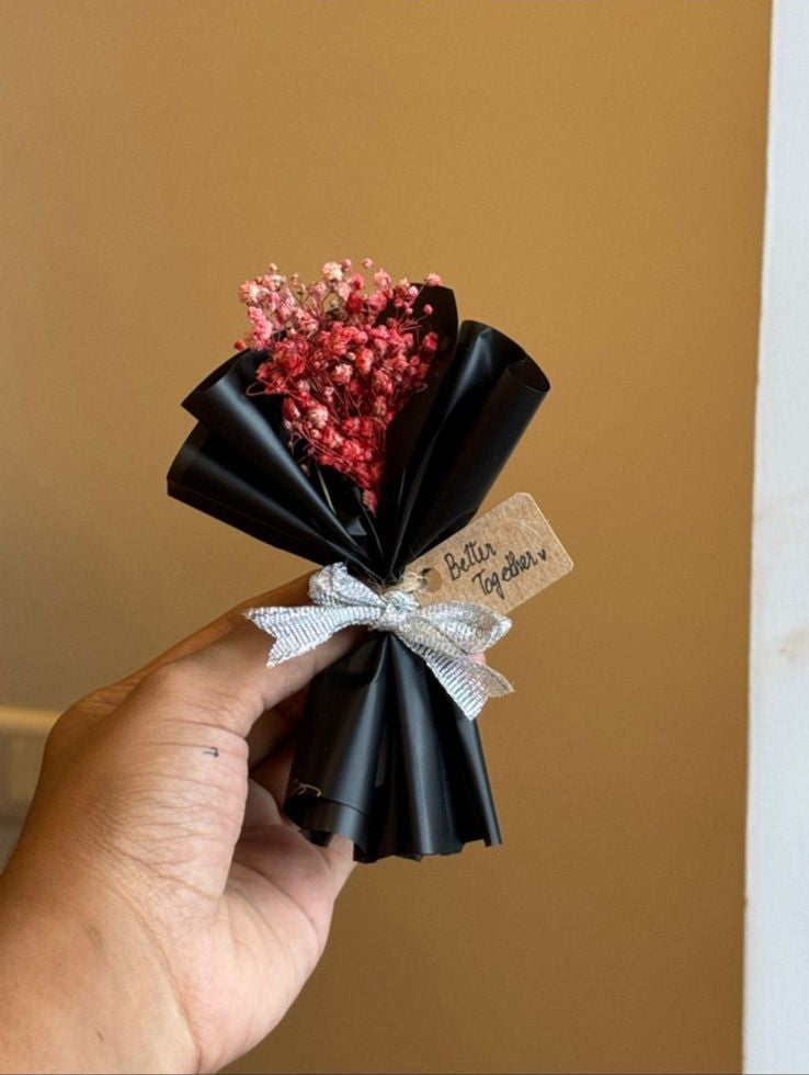 Hand holding handcrafted bouquet wrapped in black and white paper with red flowers and tag